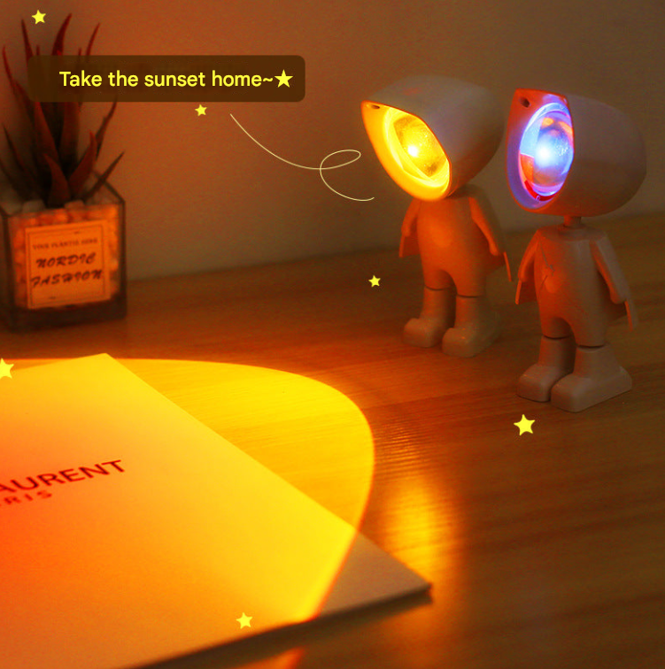 Two Mini Robot Sunset Projector Light casting a warm glow on a surface with a decorative text above.