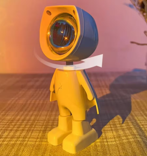 Mini Robot Sunset Projector Light with a large head and blue visor on a textured surface.